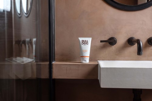 A bathroom with a sink, black faucet, and a bottle labeled "BULLDOG" on the beige countertop.