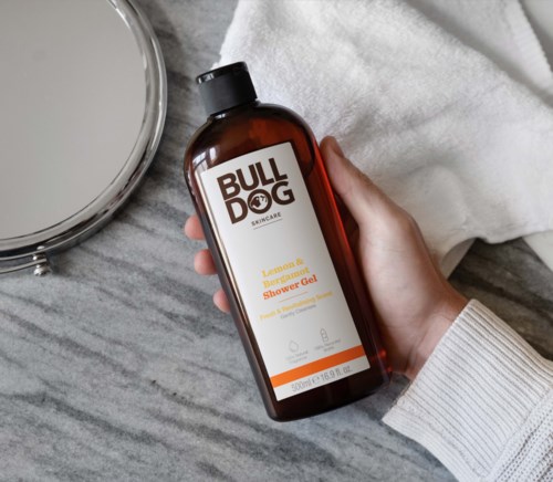 Brown bottle of Bulldog Skincare Lemon & Bergamot Shower Gel near a mirror and white towel.