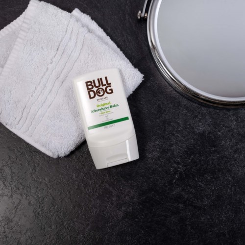 A small tube of Bulldog Aftershave Balm next to a white towel on a dark surface.