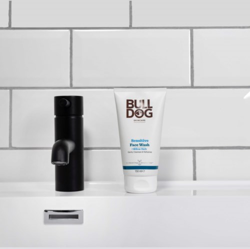 A black soap dispenser and a white tube labeled 'BULL DOG' Sensitive Face Wash on a bathroom shelf.