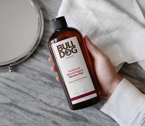 Brown bottle labeled Bull Dog Skincare, Vetiver & Black Pepper Shower Gel, on a grey surface with a mirror and towel.