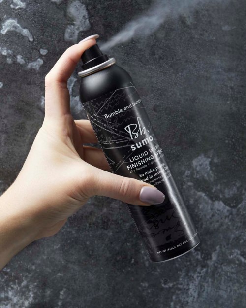 Eine Hand sprüht eine schwarze Sprühdose mit Flüssigfinish über eine dunkle Oberfläche.