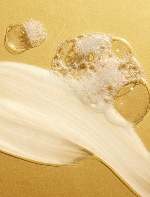 Eine weiße cremige Substanz mit Blasen schwebt über einem goldfarbenen Hintergrund, ähnlich Schaum oder Schaum.