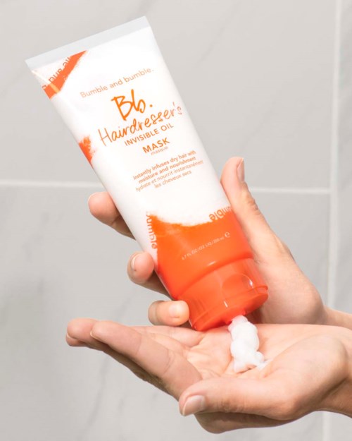Eine Person trägt eine weiße Creme aus einer Tube auf die Hand auf, die mit 'Bumble and bumble. Hairdresser's Invisible Oil Mask' beschriftet ist.