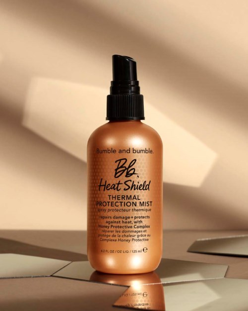 Eine braune Sprühflasche mit schwarzem Deckel, beschriftet mit 'Bumble and bumble Heat Shield Thermal Protection Mist'.