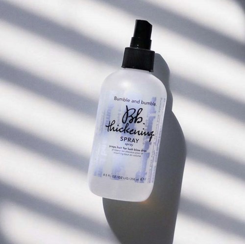 Eine weiße Sprühflasche mit den Marken 'Bumble and Bumble' und 'Thickening Spray' mit schwarzer Düse, Schatten durch Linien.