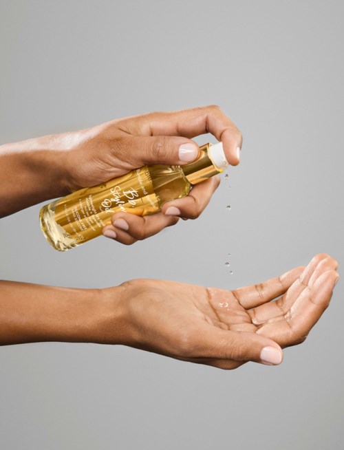 A person sprays lotion from a bottle into their open hand on a gray background.