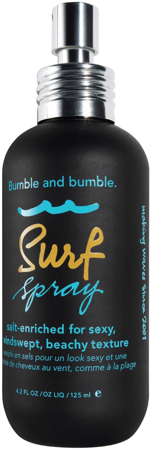 Eine schwarze Sprühflasche mit silberner Kappe, beschriftet mit 'Bumble South Surf Spray' in blauer Schrift, zeigt eine Sonne und Welle.