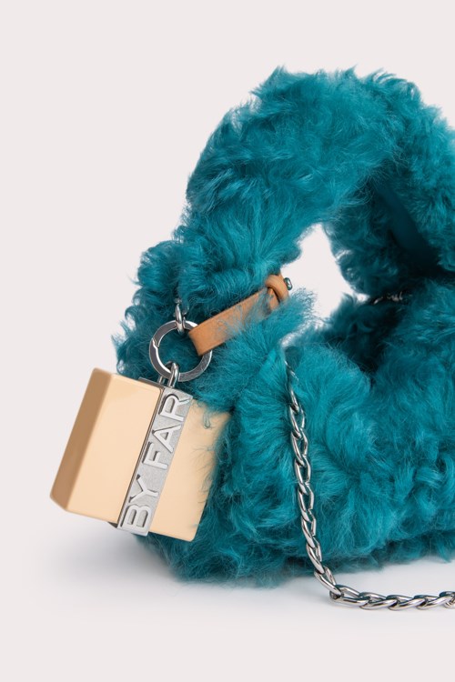 Eine flauschige blaue Handtasche mit Kette und einem beige schlossförmigen Zubehör.