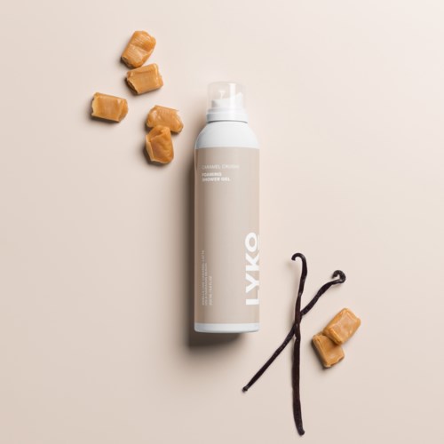 Dit is een fles huidverzorgingsproduct met karamel snoepjes en vanillebonen erop op een lichte achtergrond.