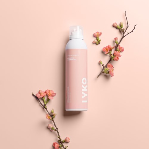 Een roze en witte fles omgeven door roze bloeiende takken op een roze achtergrond.