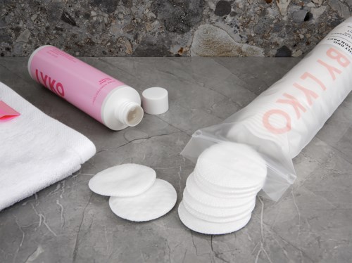 Cotton pads, a bottle of toner, and a towel on a gray surface.