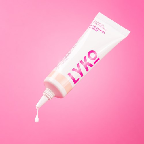 Witte tube met huidverzorgingsproduct met roze en oranje accenten, gelabeld LYKO, op roze achtergrond.
