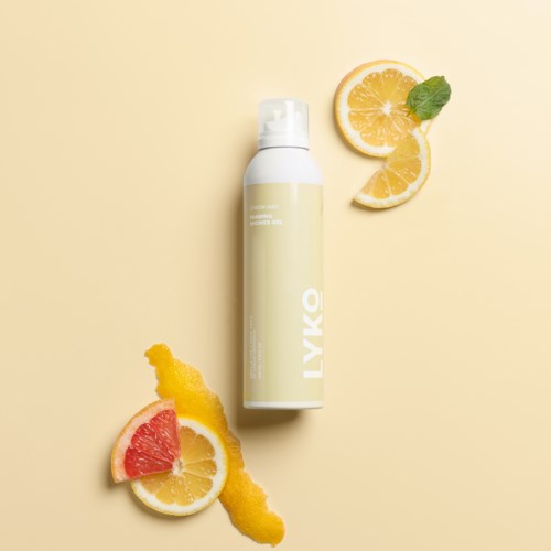 Een witte fles met LYKÓ label omgeven door citroen, grapefruit en gele citrusstukken en schil op een lichte achtergrond.