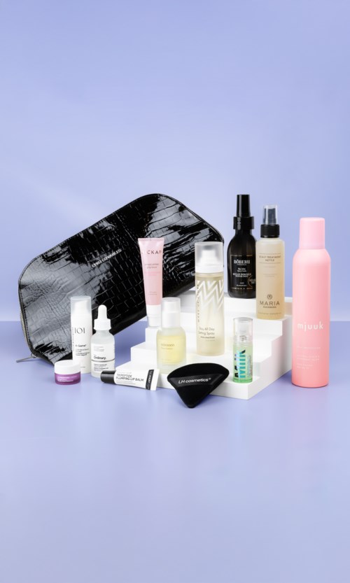 Various skincare and beauty products arranged with a black and gray patterned bag against a light purple background.