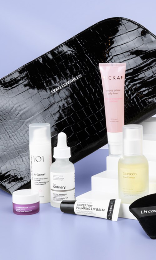 A collection of skincare and beauty products in front of a large black crocodile-patterned bag.