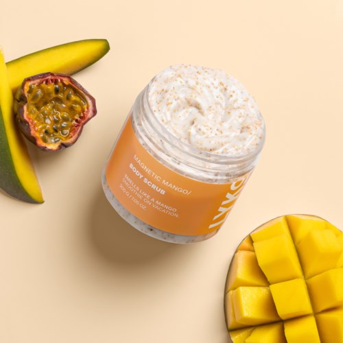 Ein Glas Mango-Body-Scrub umgeben von Bananenscheiben, Passionsfrucht und Mangowürfeln auf hellbeigem Hintergrund.