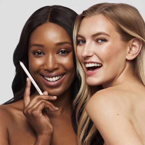 Twee vrouwen lachen blij, één houdt een make-up kwast dicht bij haar gezicht, in een vriendelijke en vrolijke scène.
