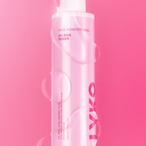 Een roze huidverzorgingsfles met label 'Pure Porefection' en '2% BHA Toner' op een roze achtergrond.