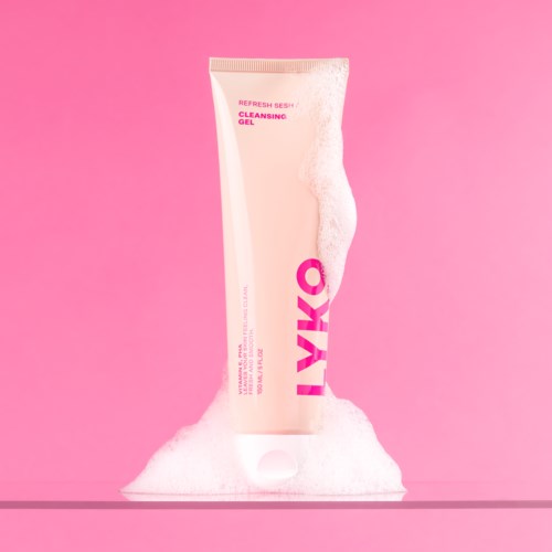 A pink tube of cleansing gel with foam around it on a pink background.
