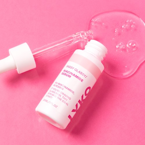 Een huidverzorgingsserumfles met pipet, ligt op een roze oppervlak met wat serum dat is gemorst en bellen.