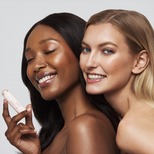 Twee vrouwen met glad huid, één met donker haar en de ander met blond haar, glimlachen en houden een huidverzorgingsproduct.