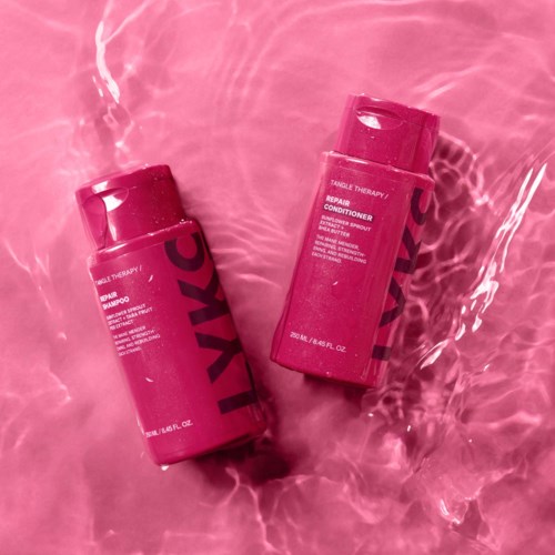 Twee roze flessen haarverzorgingsproducten drijven in het water, een gemarkeerd 'Shampoo' en de andere 'Conditioner.'
