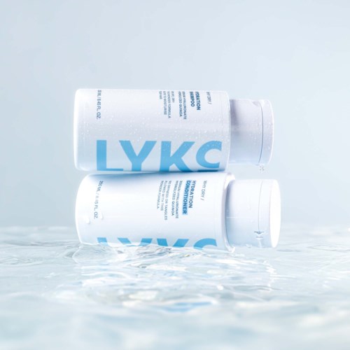 Twee witte flessen met LYKC liggen op een vochtige ondergrond met water eromheen.