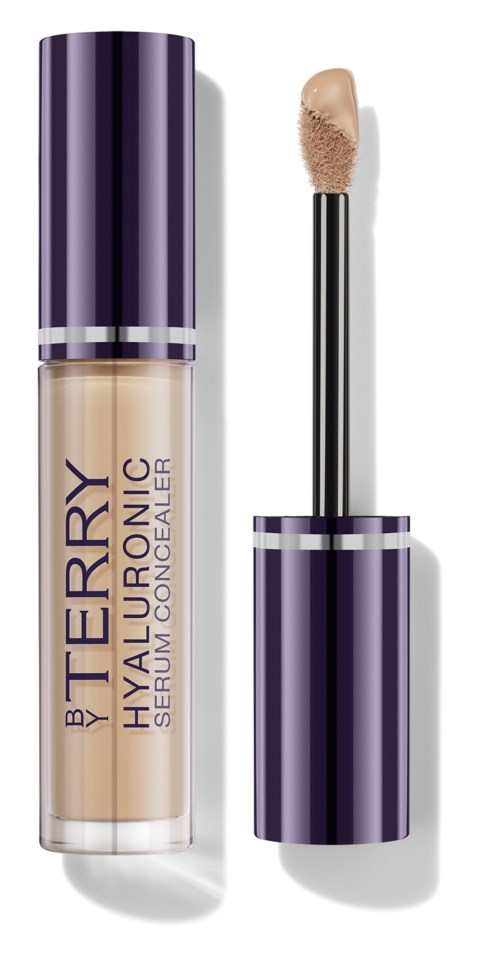 Peiteainepullon, jonka kansi on violetti, ja siinä lukee 'by Terry Hyaluronic Serum Concealer,' sekä sivellin vieressä.