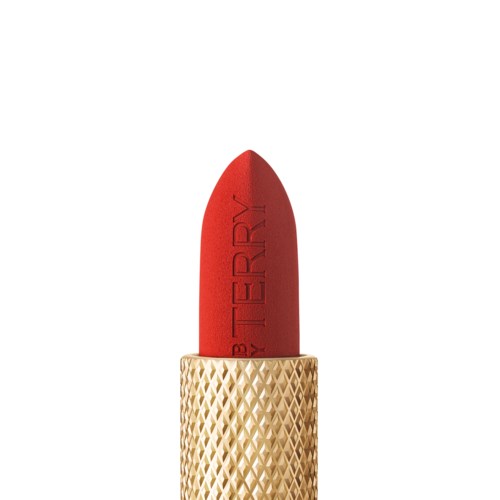 A red lipstick with gold textured case. The lipstick is standing upright and titled to show the product name.