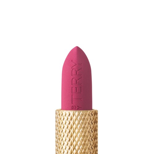 A pink lipstick with a gold, textured case, standing upright. The lipstick has the words "BE TERRY" engraved on it.