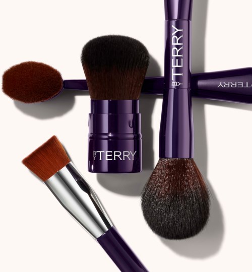 A set of makeup brushes in purple handles, with various brush shapes and sizes. Some have brown or black bristles.