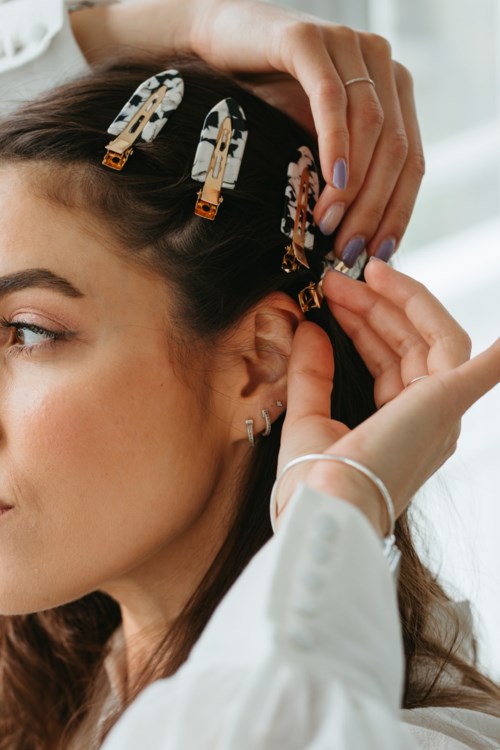 Eine Frau benutzt Haarspangen, um ihre Haare zu sichern, während sie eine Klammer anpasst und andere Clips im Haar sichtbar sind.