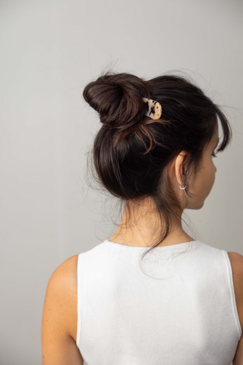 A woman with dark hair in a messy bun, wearing a white sleeveless top, facing away and to the side.