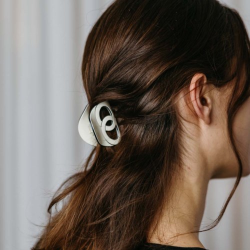 A woman has a large, white, wireless headphone on her hair. She has long, brown hair and is facing sideways.
