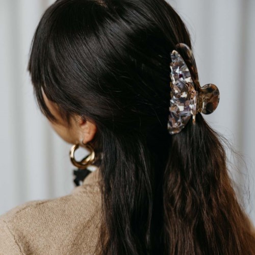 Eine Frau mit langen dunklen Haaren trägt große goldene Creolen und einen großen Schmetterlings-Haarclip.