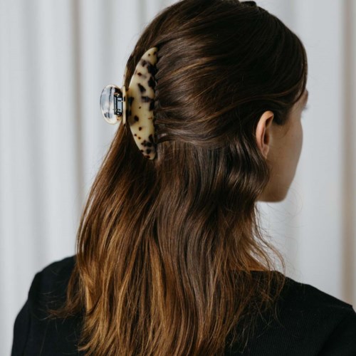 A woman has a large spotted hair clip securing her brown hair styled with loose waves.