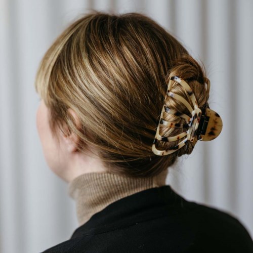 Een vrouw met lichtbruin haar in een dot, vastgemaakt met een grote, gekleurde haarclip.