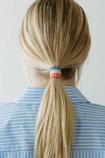 Een vrouw met blond haar in een paardenstaart, vastgebonden met een rood, wit en blauw haarband, van achteren.