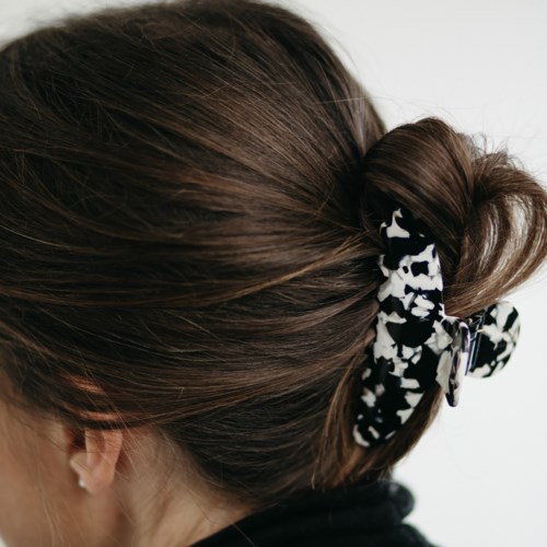 Eine Frau mit braunem Haar, das mit einem schwarz-weißen Musterhaarband zusammengebunden ist.