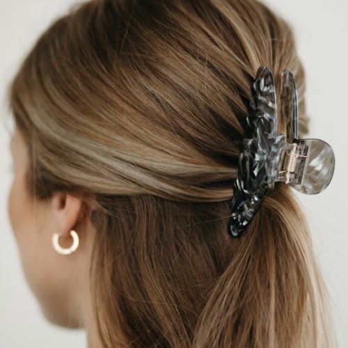 A woman with light brown hair wearing a black and white patterned hair claw clip and gold hoop earrings.
