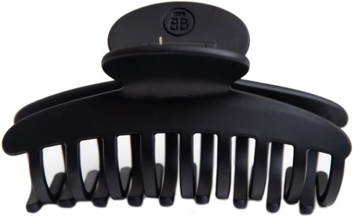 A large black hair clip with many teeth and a rounded top section, sitting on a white surface.