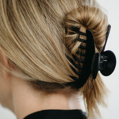A person with blonde hair tied in a bun uses a black hair clip to hold their hair back.