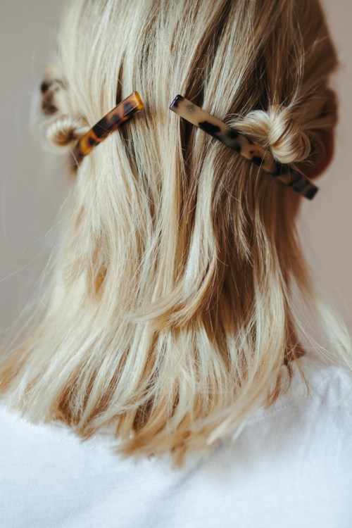 Eine Person hat blondes Haar mit zwei Schildpatt-Haarspangen, leicht gewellt und hinten gebunden.