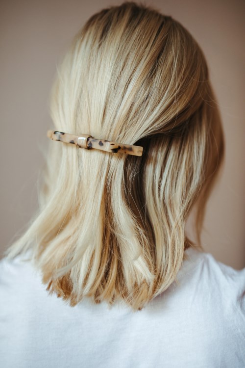 Eine Frau mit blonden Haaren, die mit einem kleinen, beigen und braunen Haarklammer zurückgehalten werden, trägt ein weißes Top.