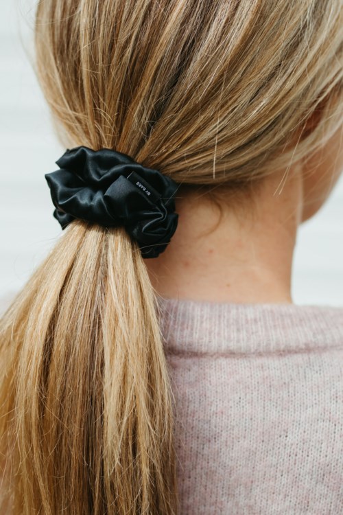 Ein Mädchen mit blondem Haar, das mit einem schwarzen Haargummi zusammengebunden ist, trägt ein hellrosa Oberteil.