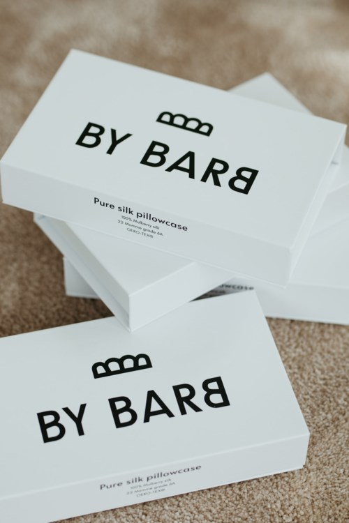 Zwei weiße Boxen mit der Aufschrift 'BY BARD' enthalten Seidenkissenbezüge, auf einer beigefarbenen Oberfläche.