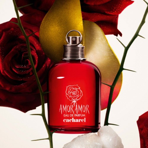 A red perfume bottle with a silver cap surrounded by red roses and a green leaf. A golden heart is in the background.