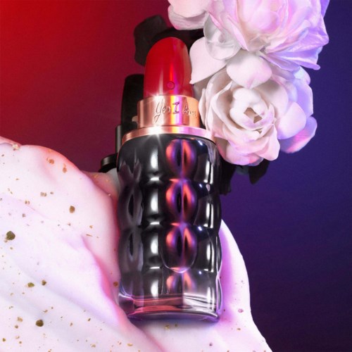Lipstick with decorative black bottle, surrounded by white roses and pink and white fluffy fabric.