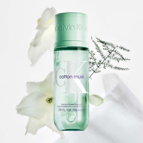 En flaske Calvin Klein Cotton Musk-parfyme med hvite blomster og grønne blader rundt den.